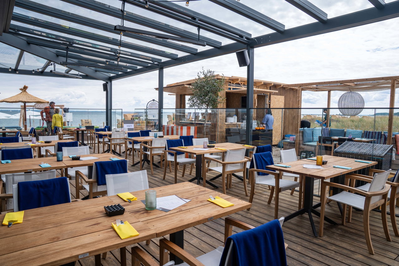 Überdachte Terrasse mit eingedeckten Tischen und Sonnenschirmen
