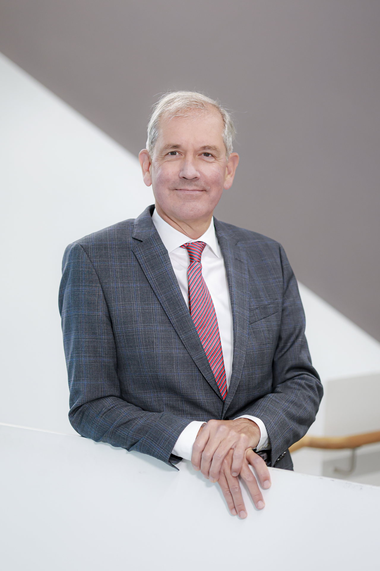 Professor Dr. Jens Scholz im grauen Anzug mit roter Krawatte an einem weißen Treppengeländer