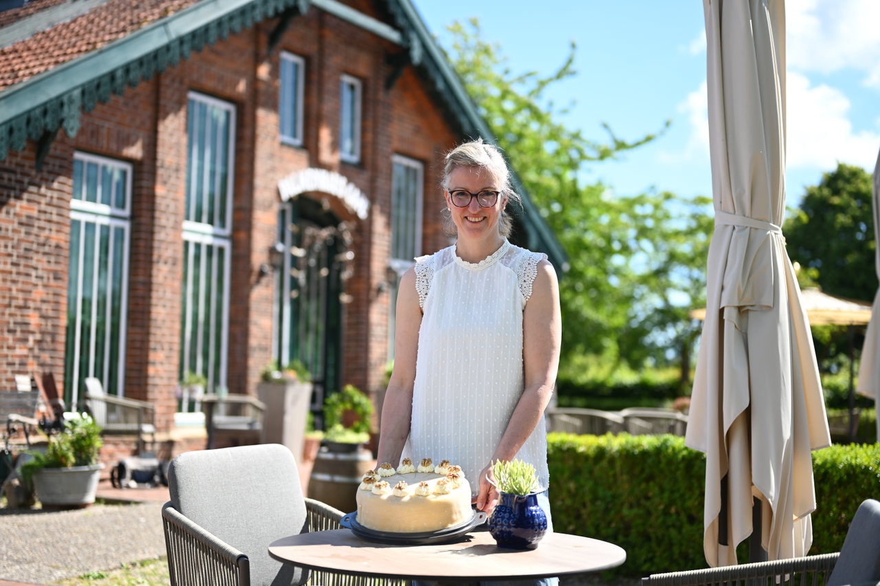 Pächterin mit selbstgebackener Torte an einem Tisch vor dem Café im historischen Backsteingebäude