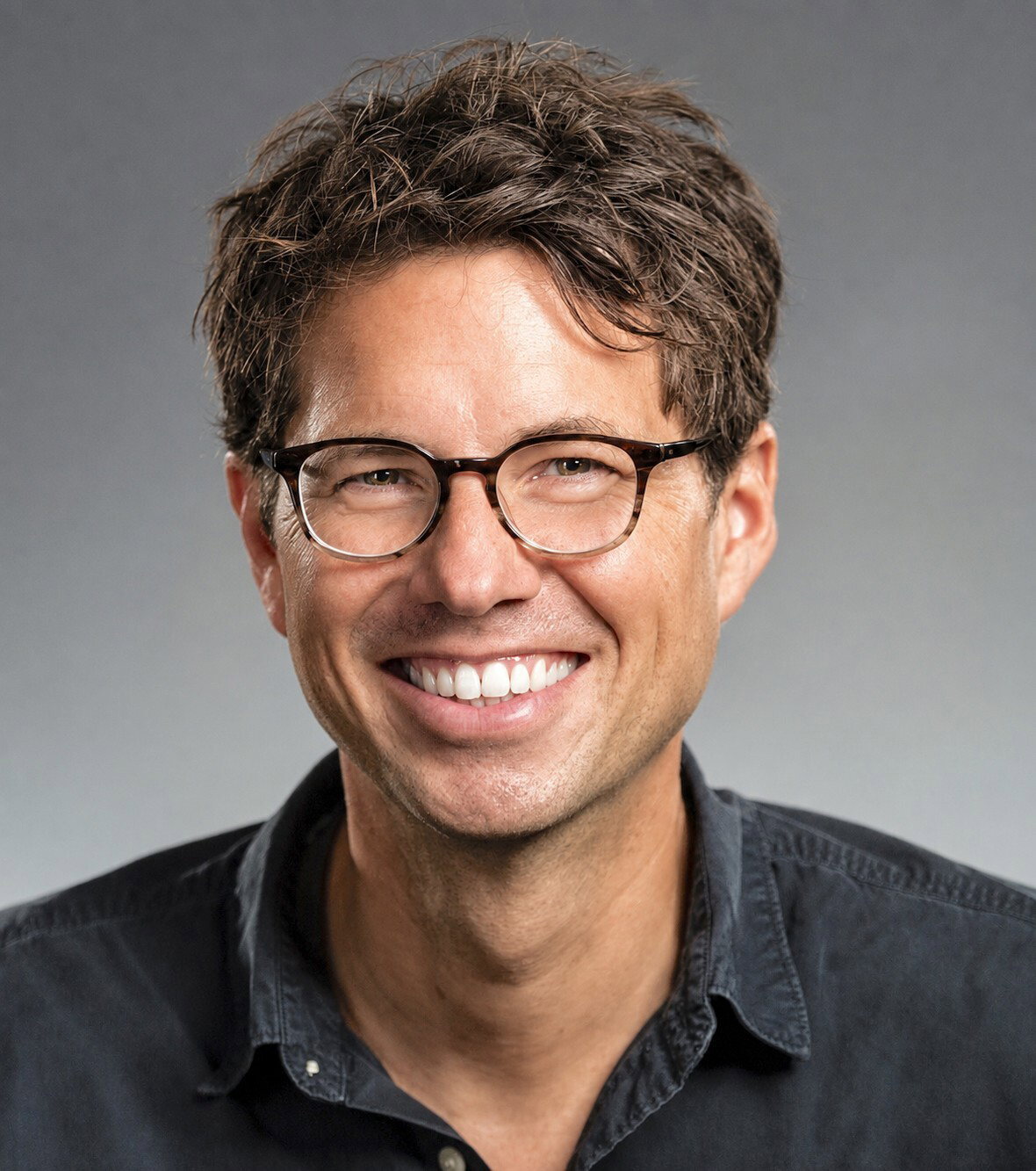Porträt von Stefan Vochezer mit Brille und dunklem Hemd vor grauem Hintergrund