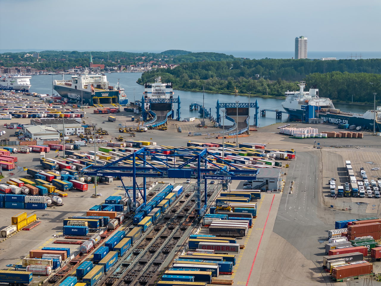 Terminal am Skandinavienkai mit blauer Kranbrücke über Gleisen, Containern und Trailern, im Hintergrund Fähren
