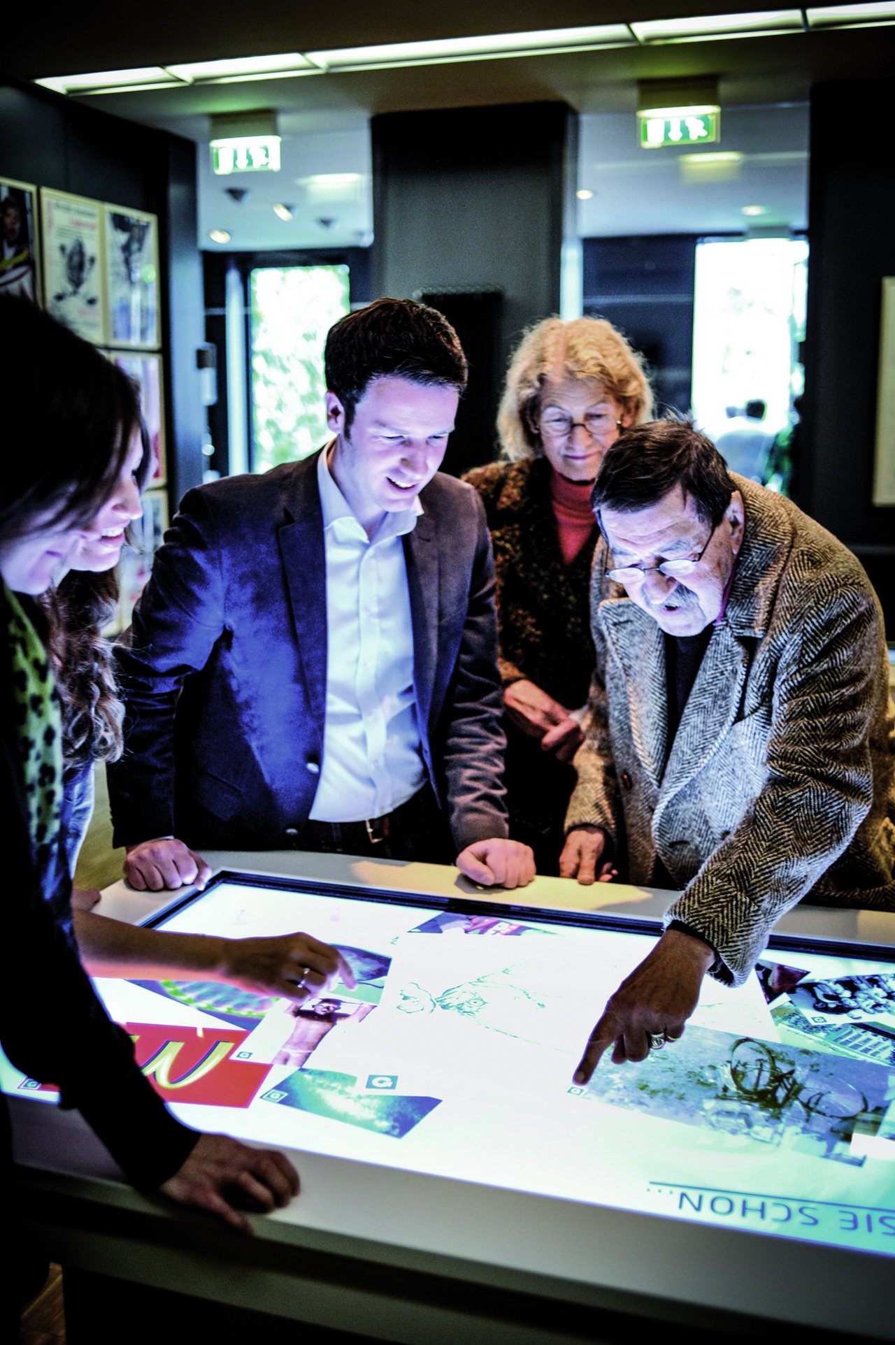 Günter Grass und Dr. Jörg-Philipp Thomsa beugen sich mit Besucherinnen über einen beleuchteten Medientisch im Museum