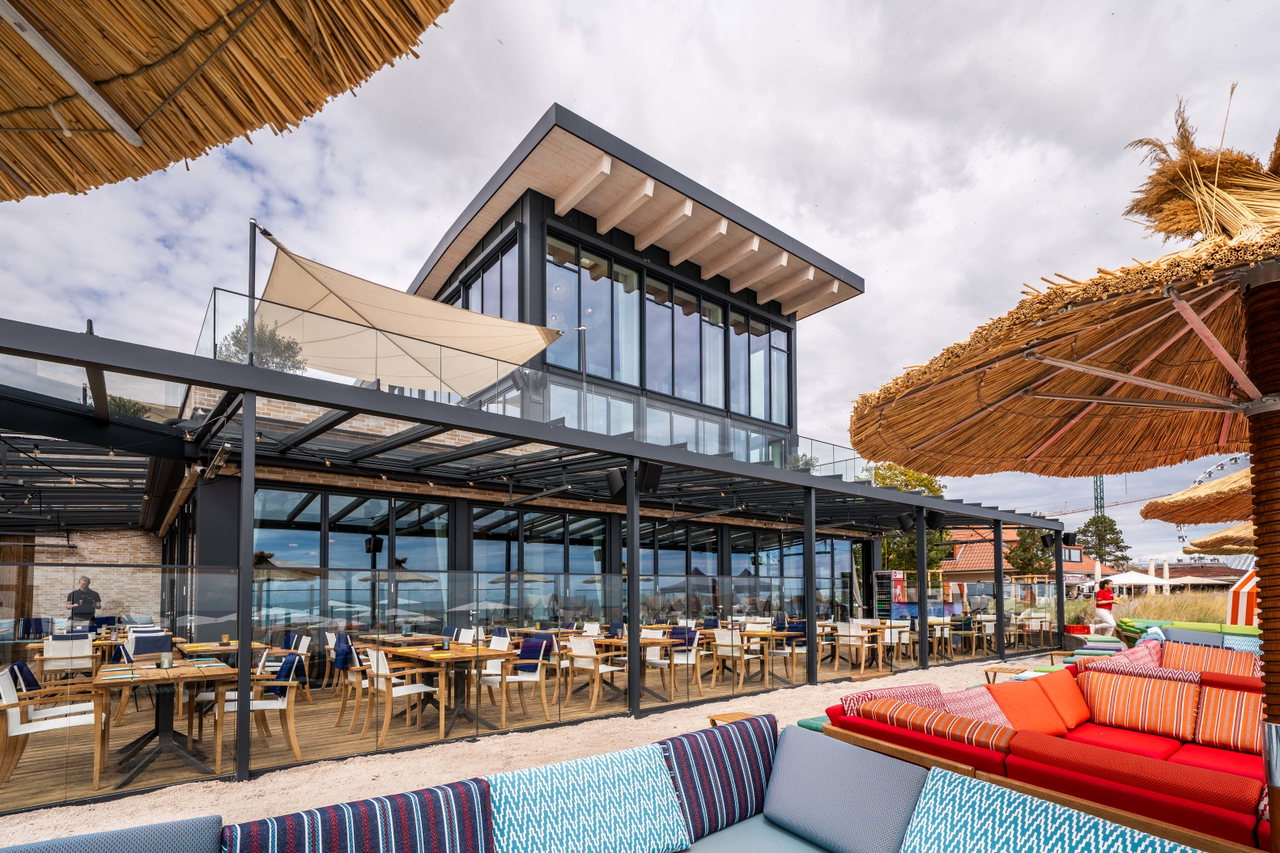 Strandnahe Restaurantterrasse mit Reetschirmen und farbigen Sitzbänken