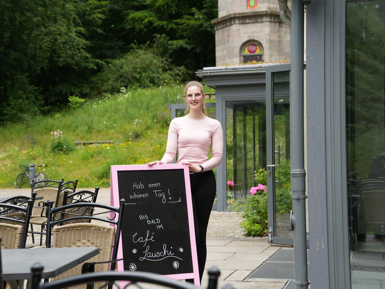Pächterin des Café Lauschi mit beschriebener Angebotstafel vor dem Lokal