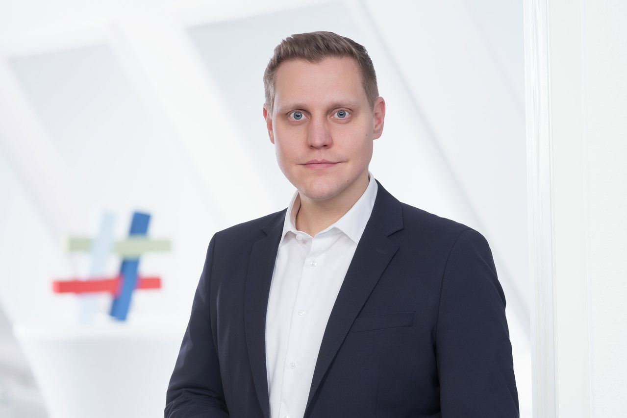 Julius Krüger, Referent für Verkehr, Infrastruktur und Mobilität bei der IHK zu Lübeck, im dunklen Sakko vor heller Wand
