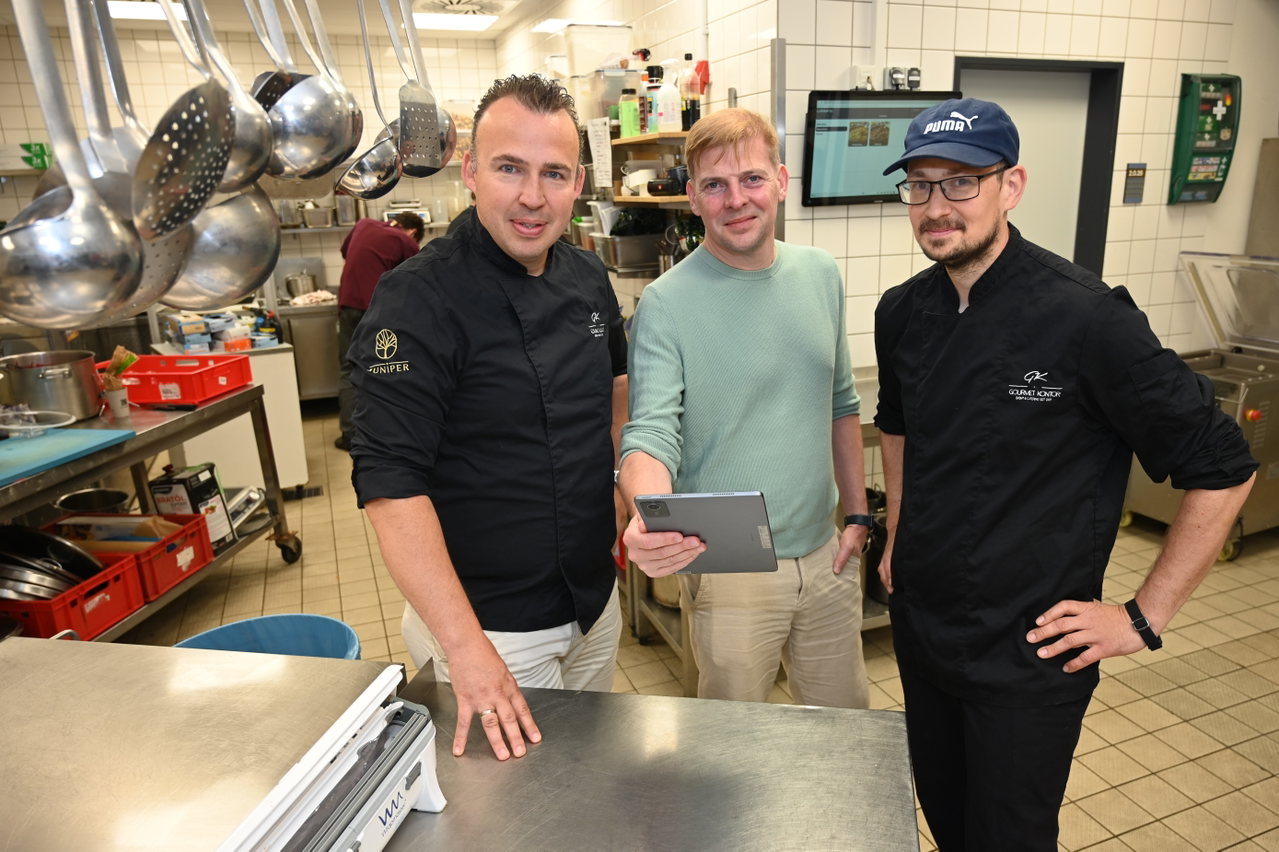 Drei Mitarbeiter in einer Gastronomieküche, einer von ihnen hält ein Tablet in der Hand