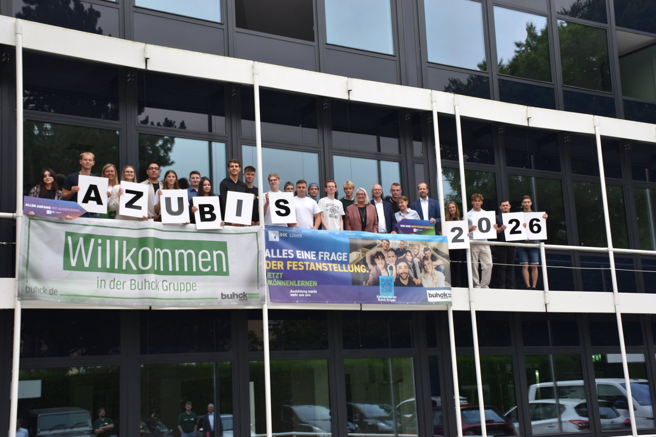 Auszubildende und duale Studierende der Buhck Gruppe halten auf einer Galerie vor der Glasfassade Schilder mit „AZUBIS 2026“, darunter ein Willkommensbanner