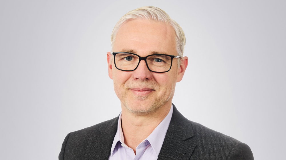 Porträt von Dr. Gunnar Pietzner mit Brille im dunklen Sakko vor hellgrauem Hintergrund
