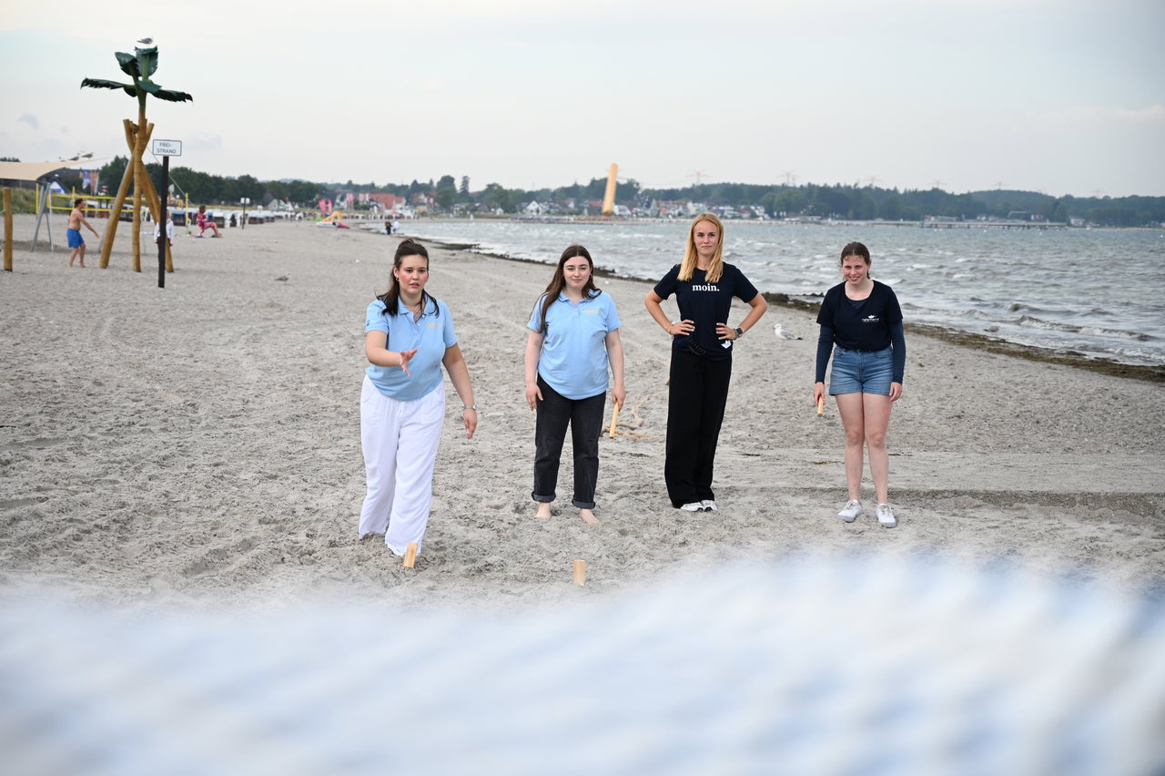 Vier junge Frauen spielen am Strand ein Wurfspiel, im Hintergrund die Ostsee
