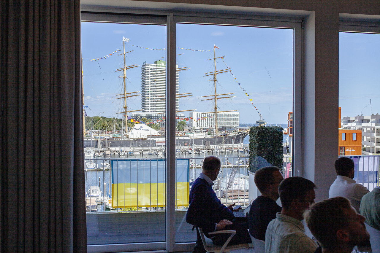 Gäste vor einem großen Fenster mit Blick auf die Passat und den Travemünder Hafen