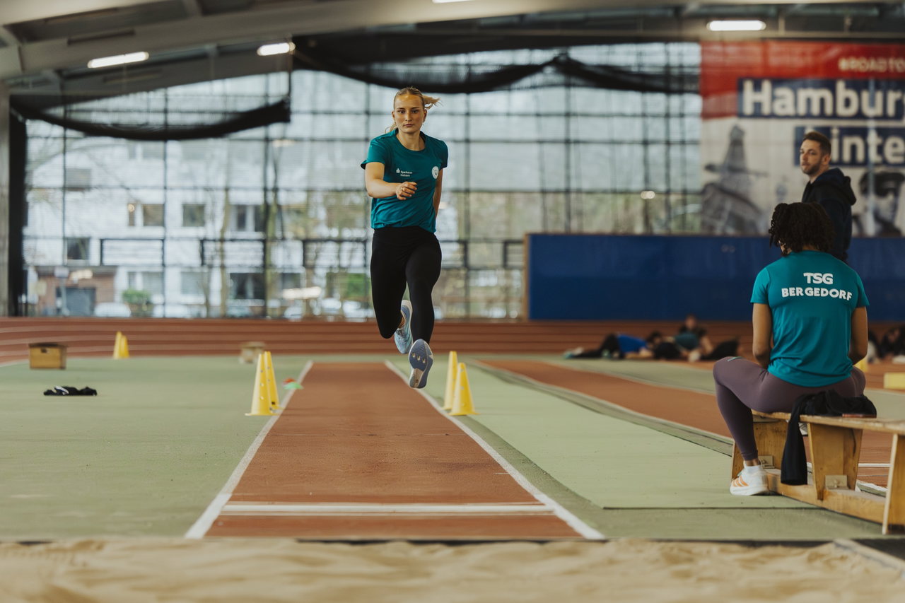 Weitspringerin im Anlauf auf der Bahn in einer Leichtathletikhalle