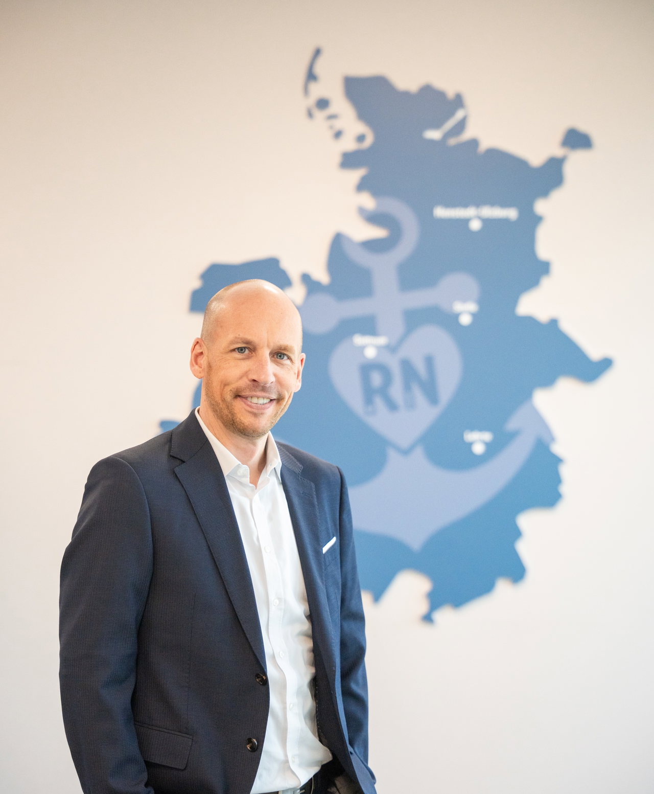 Andreas Persigehl im dunklen Sakko vor einer Wandgrafik mit der Karte der REWE Region Nord