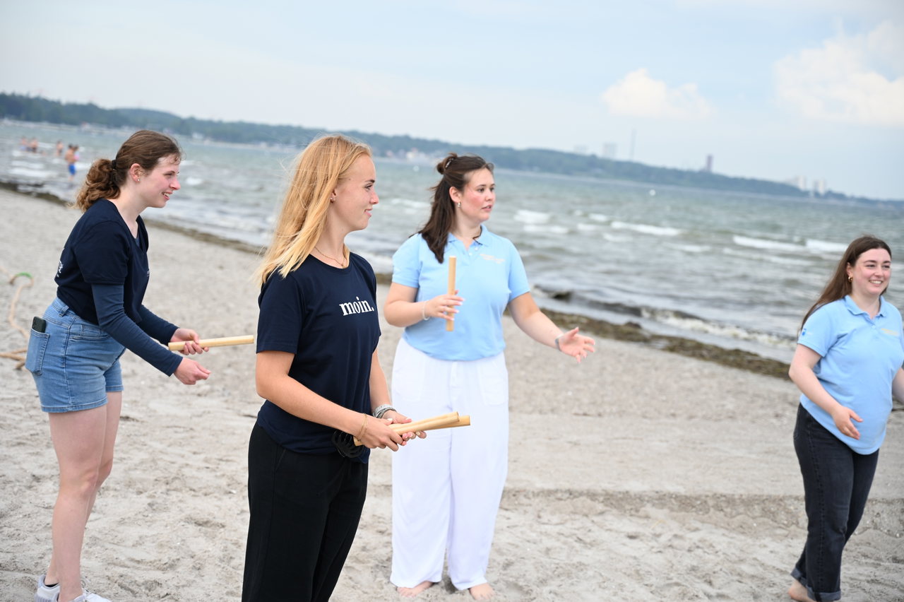 Jugendliche und Polizistinnen bei einem Wurfspiel mit Holzstäben am Strand