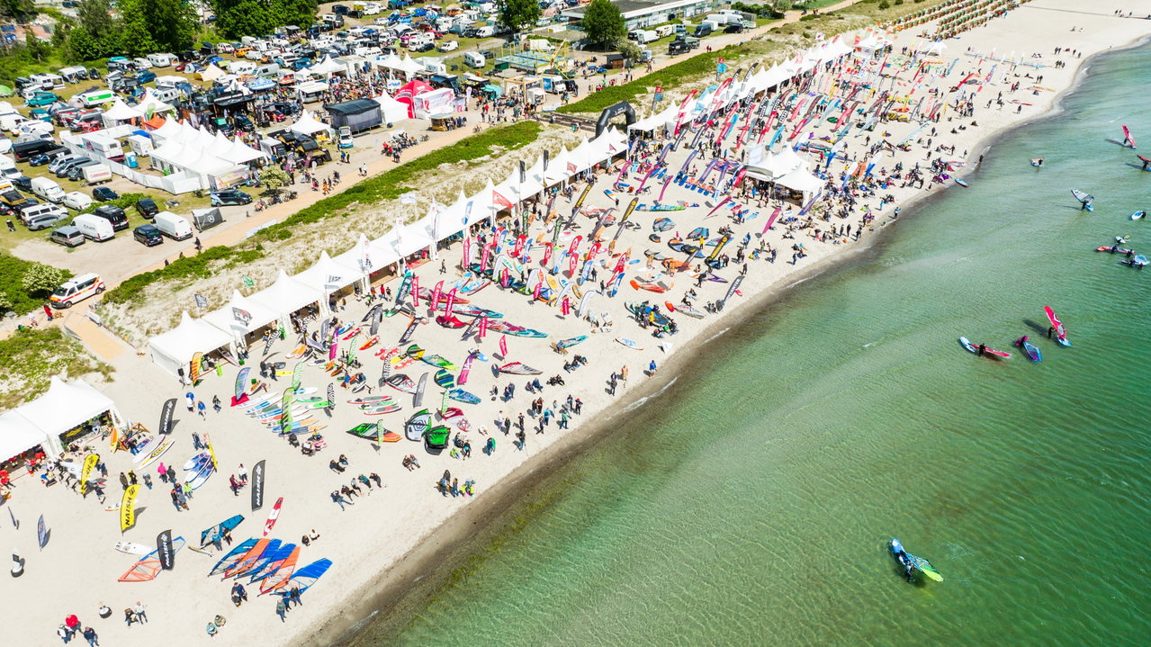 Luftaufnahme des Surf-Festivals Fehmarn mit Zelten, Surfbrettern und Segeln am Strand
