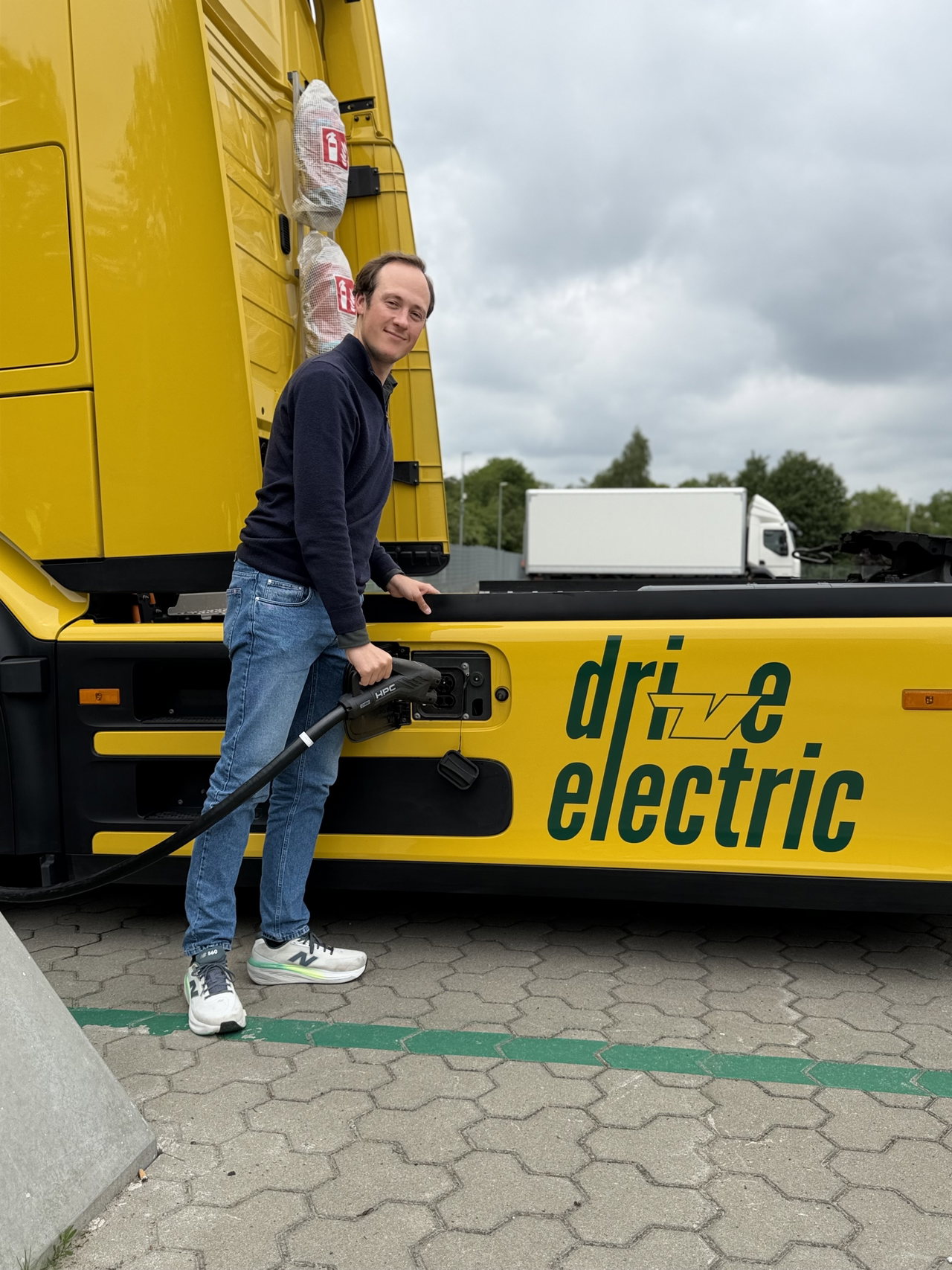 Hannes Voigt steckt den Ladestecker in einen gelben E-Lkw mit der Aufschrift „drive electric“