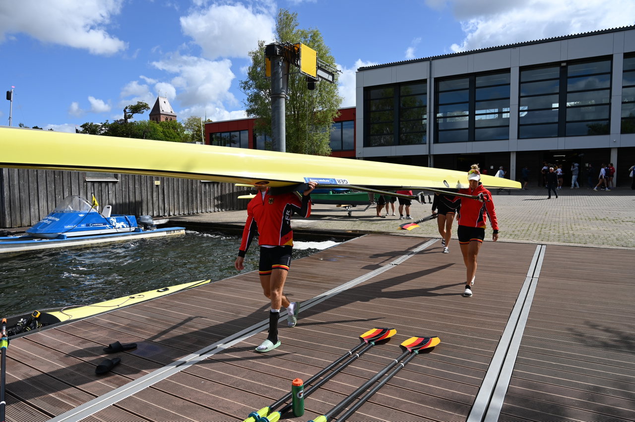 Ruderinnen tragen ein gelbes Boot über den Steg vor der Ruderakademie Ratzeburg
