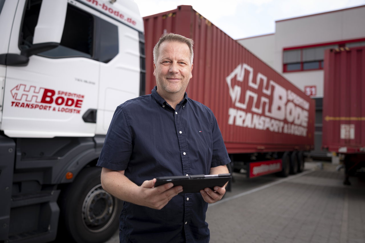 Stev Etzrodt steht mit einem Tablet vor einem Lkw und einem Container-Trailer der Spedition Bode