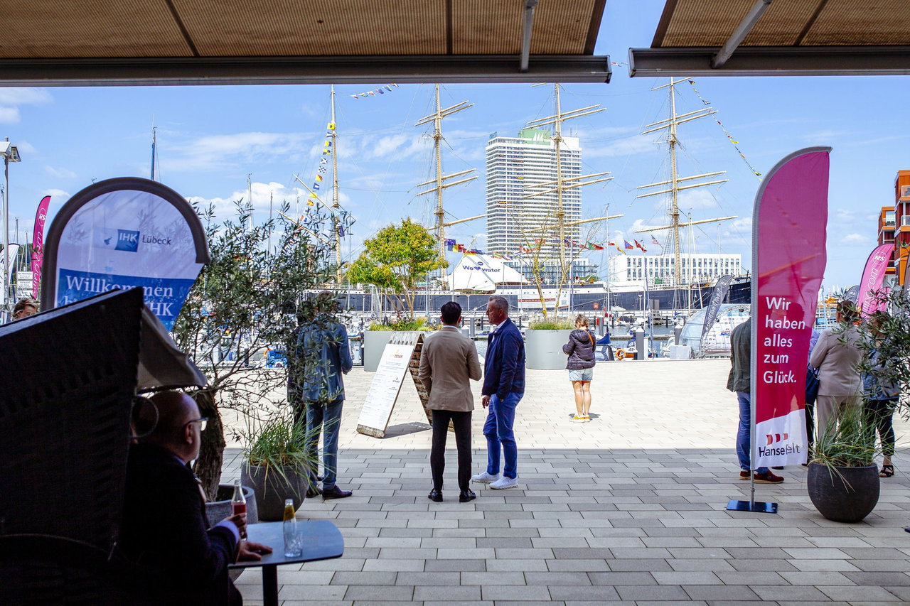 Gäste auf der Promenade in Travemünde mit Beachflags, im Hintergrund die Viermastbark Passat und das Maritim-Hochhaus