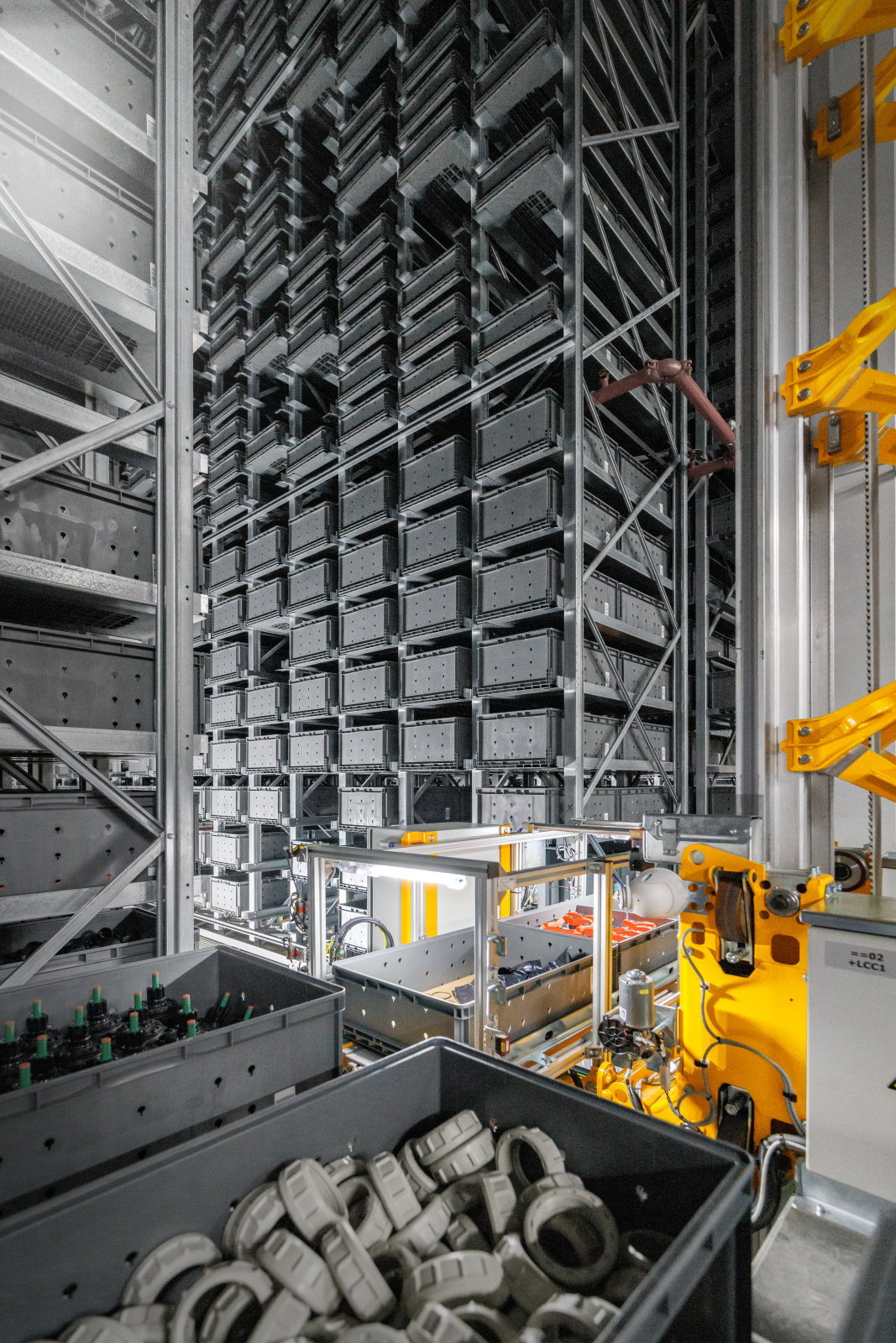 Automatisiertes Kleinteilelager mit gestapelten grauen Behältern und einem Kommissionierarbeitsplatz