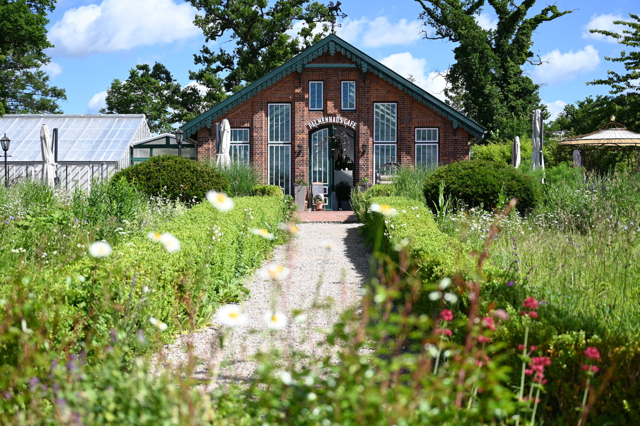Blühender Gartenweg, der auf das historische Palmenhaus auf Gut Sierhagen zuführt