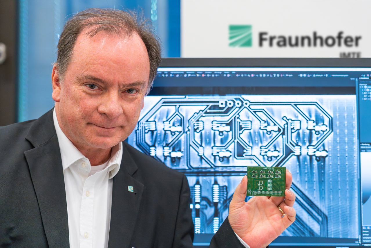 Professor Dr. Thorsten M. Buzug mit einer Leiterplatte vor einem Monitor, der deren CT-Aufnahme zeigt