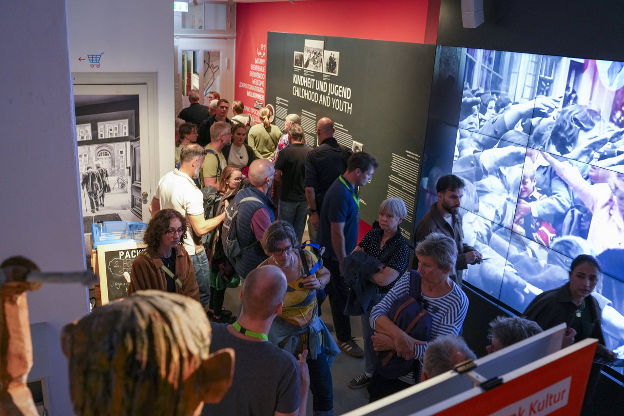 Besucherinnen und Besucher in der Ausstellung „Kindheit und Jugend“ vor einer großen Videowand