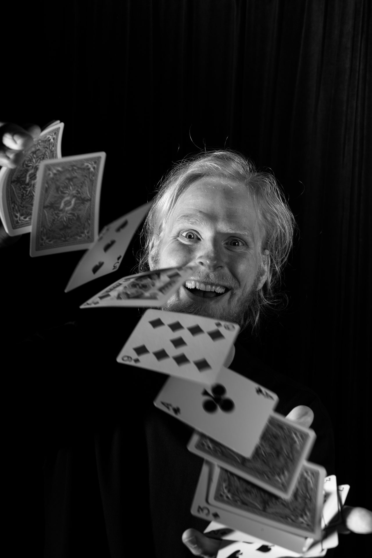 Ein Mann vor schwarzem Hintergrund, der Spielkarten fliegen lässt