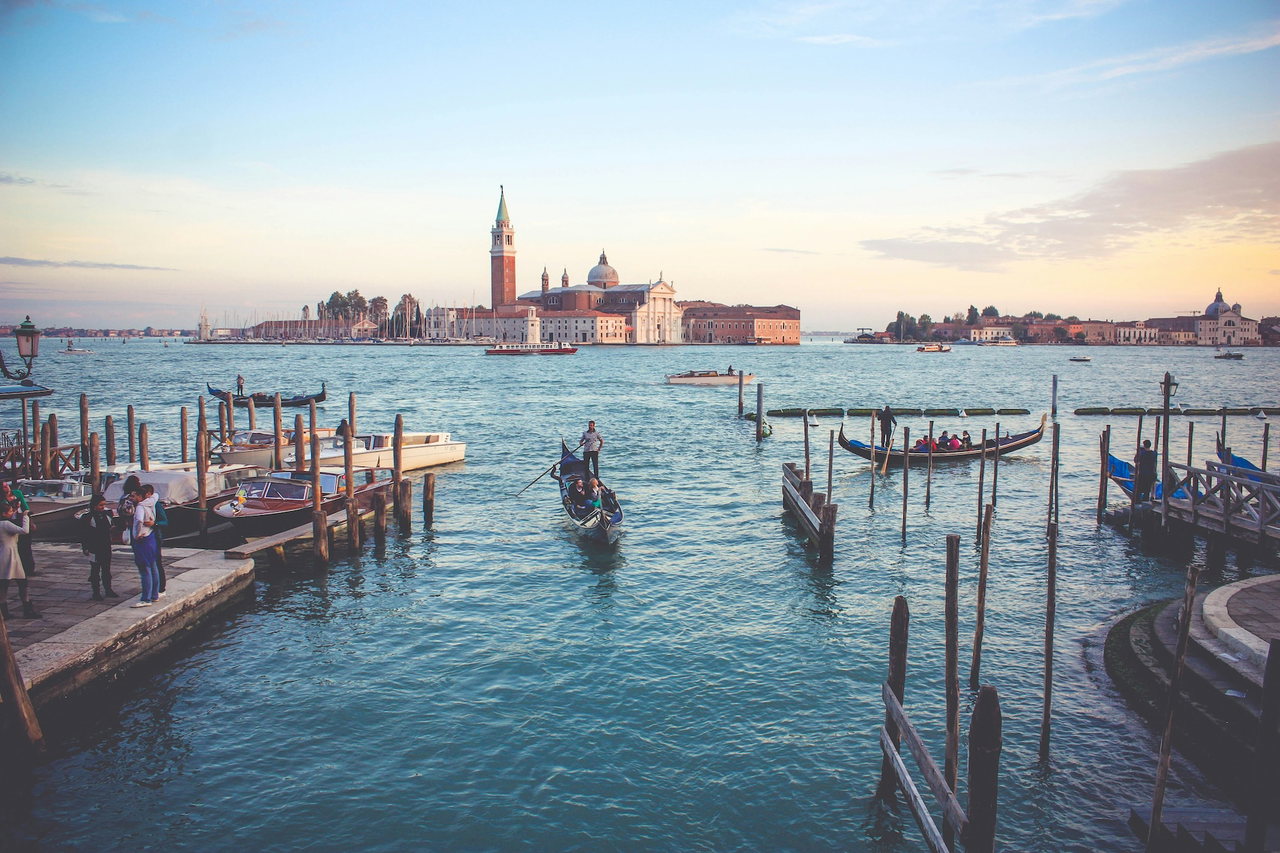 Blick über die Lagune von Venedig auf San Giorgio Maggiore, davor eine Gondel und Anlegepfähle im Abendlicht