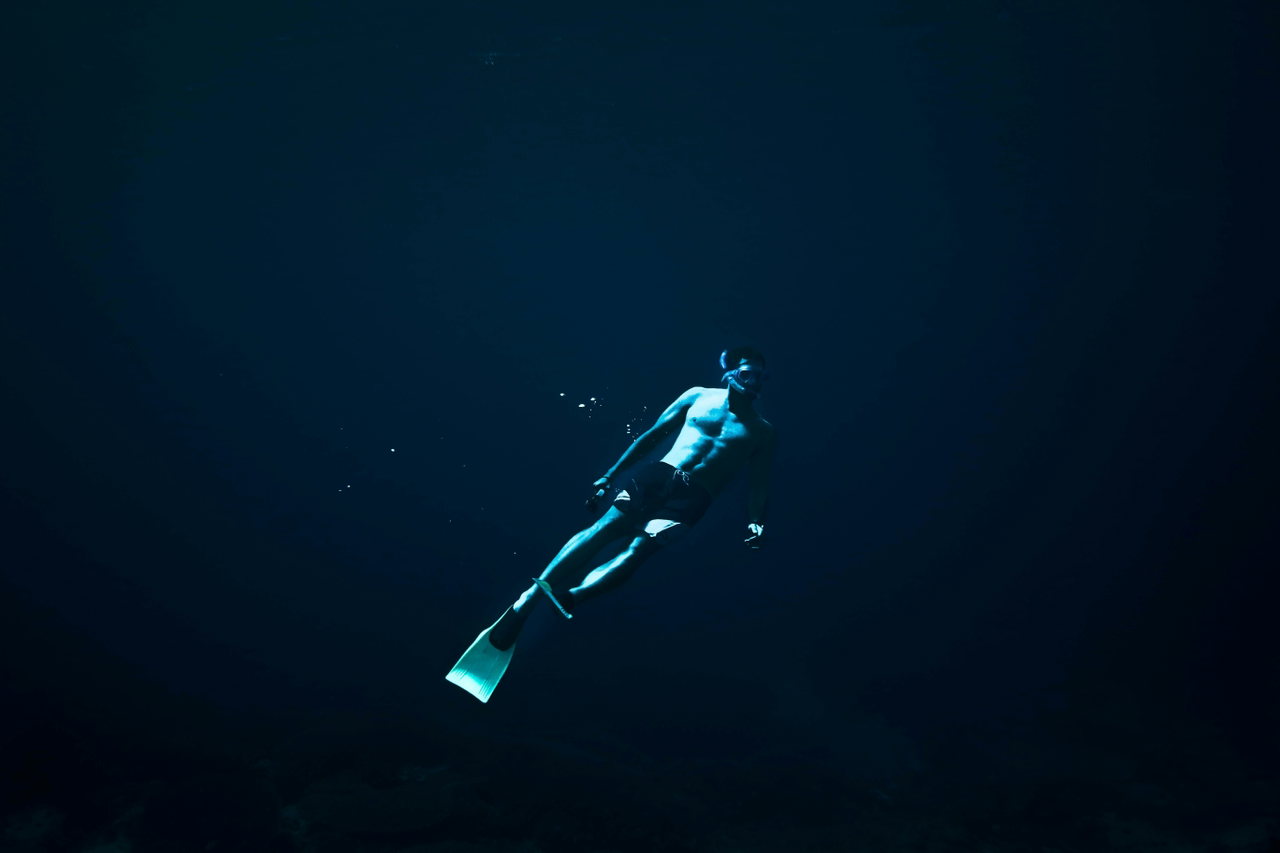Ein Freitaucher mit türkisfarbenen Flossen schwebt im dunklen Blau