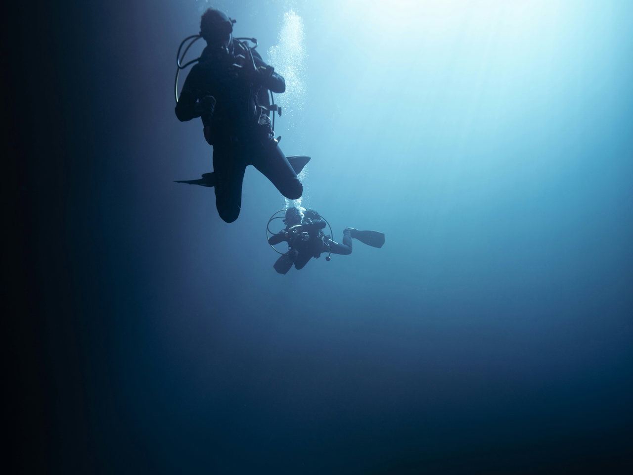 Zwei Gerätetaucher als Silhouetten im Gegenlicht unter der Wasseroberfläche