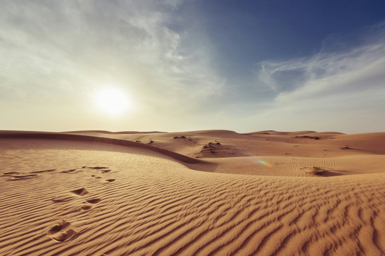 Wüste mit Fußspuren im Sand und tief stehender Sonne