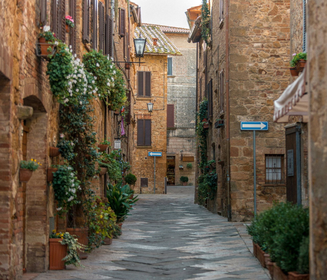 Schmale Gasse mit Natursteinhäusern und blühenden Kletterpflanzen