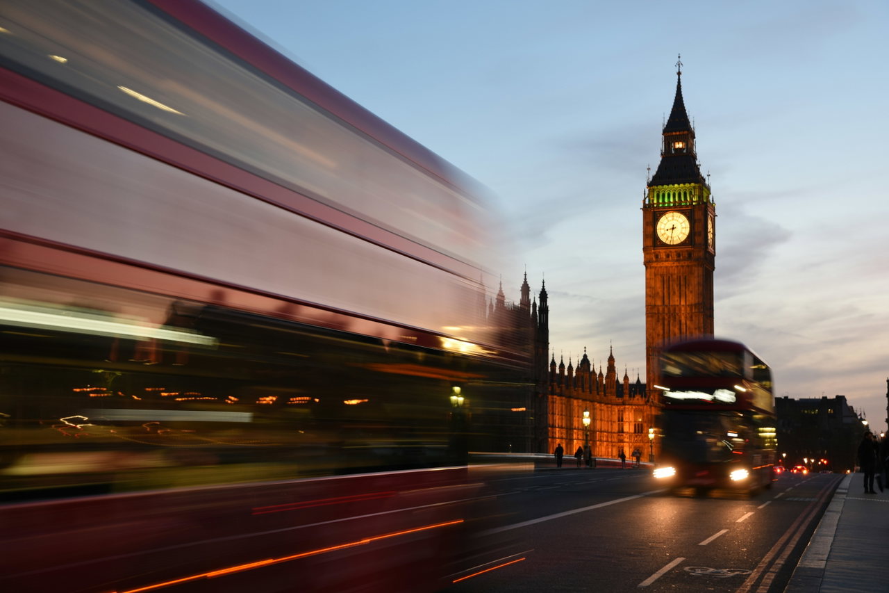 Roter Doppeldeckerbus in Bewegungsunschärfe vor Big Ben in der Abenddämmerung