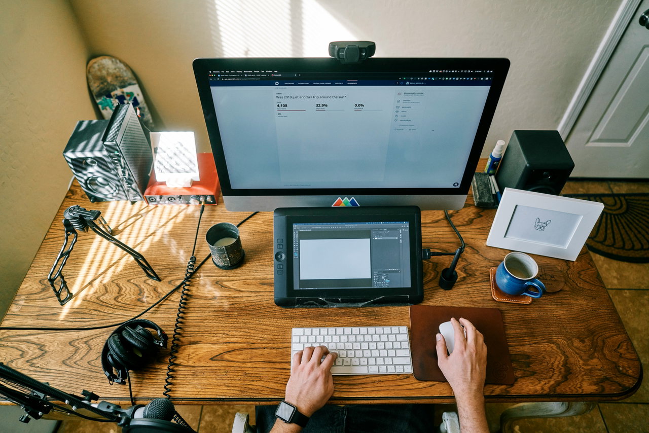 Blick von oben auf einen Holzschreibtisch mit Monitor, Grafiktablett, Tastatur und Kopfhörern