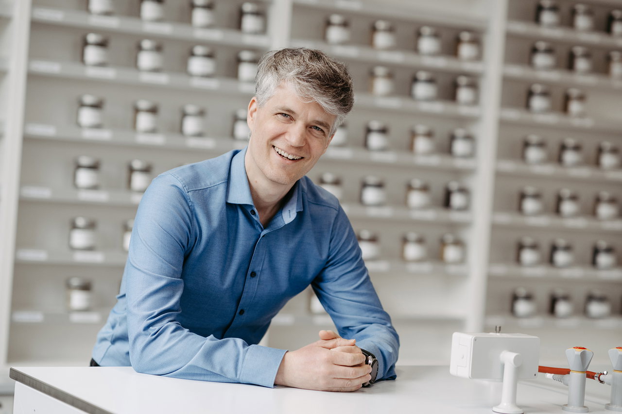Pharmakognost Andreas Koeberle sitzt vor einer Regalwand voller Arzneimittel-Fläschchen.