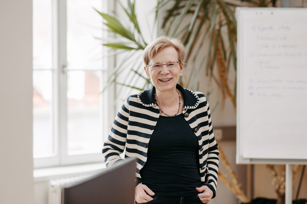 Manuela Paechter steht vor einer Pflanze und einer Flipchart in ihrem Büro