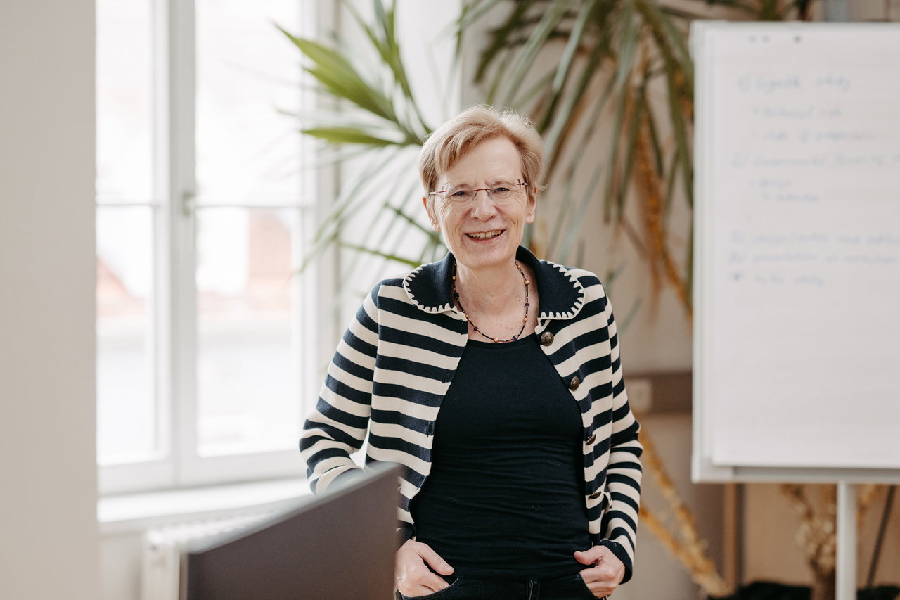 Manuela Paechter steht vor einer Pflanze und einer Flipchart in ihrem Büro