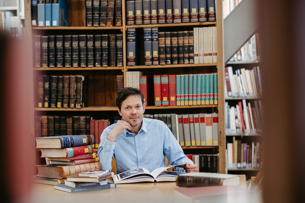 Kunsthistoriker Robert Felfe sitzt eingerahmt von Büchern in der Bibliothek des Instituts für Kunstgeschichte der Universität Graz