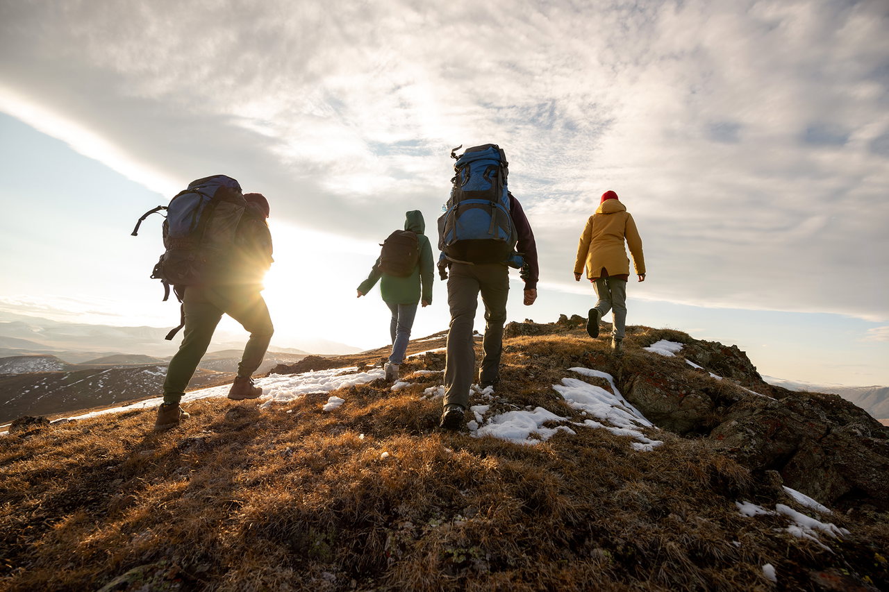 Gruppe von Wandernden, die der Sonne entgegen auf eine Kuppe zugehen