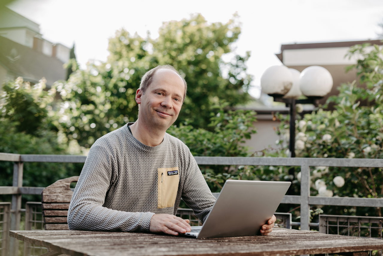 Tobias Stern sitzt vor seinem Laptop auf der Terrasse seines Instituts, im Hintergrund sind Büsche.