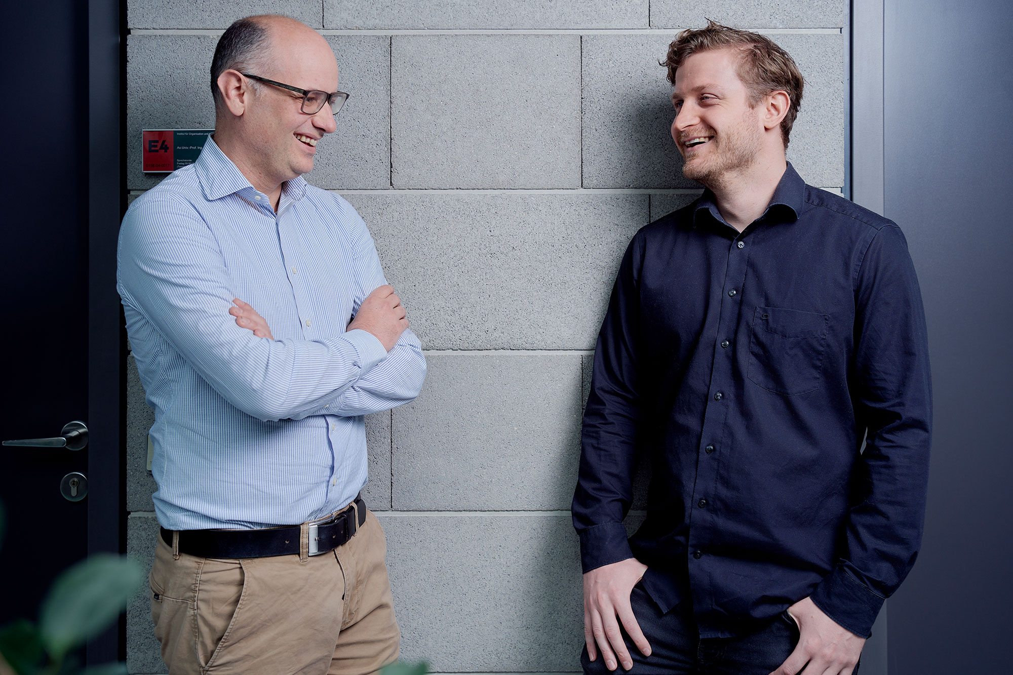 Jürgen Fleiß und Armin Haberl lachend im Gespräch miteinander vor Bürotüren im RESOWI-Zentrum der Uni Graz