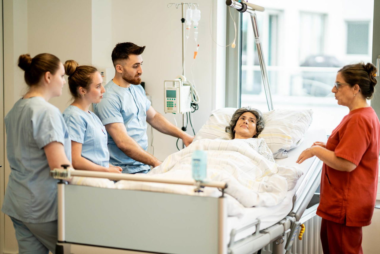 Studierende der Gesundheits- und Krankenpflege üben mit einer Lehrenden am Patientenbett im Skills Lab