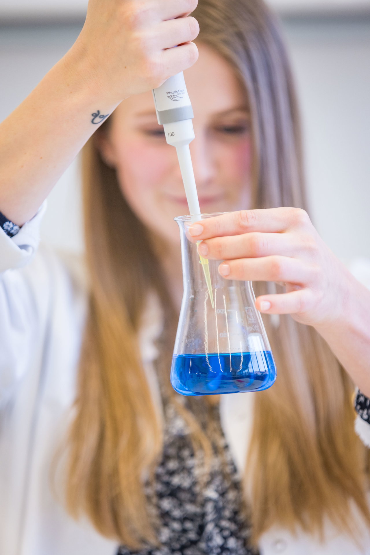 Studentin pipettiert eine blaue Flüssigkeit in einen Messkolben