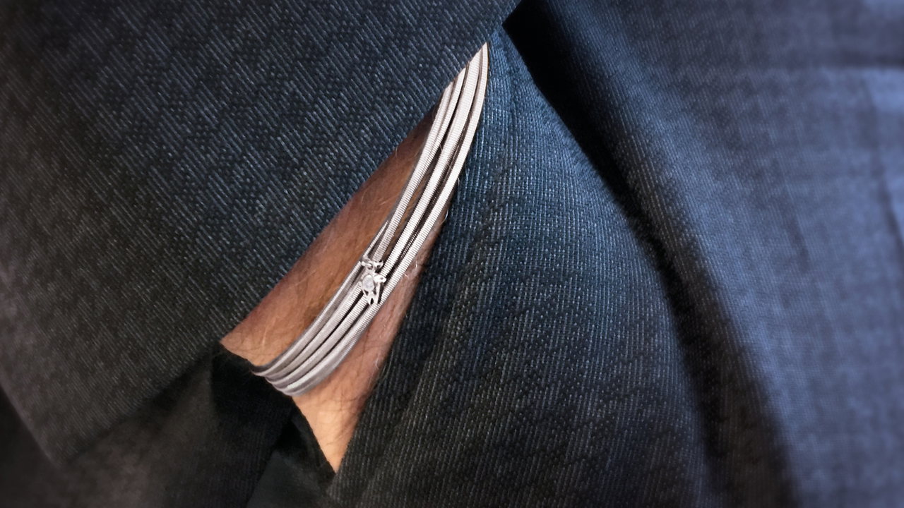 Nahaufnahme des Handgelenks eines Mannes mit Armband PURES GLÜCK in Weißgold unter einem dunklen Anzugärmel