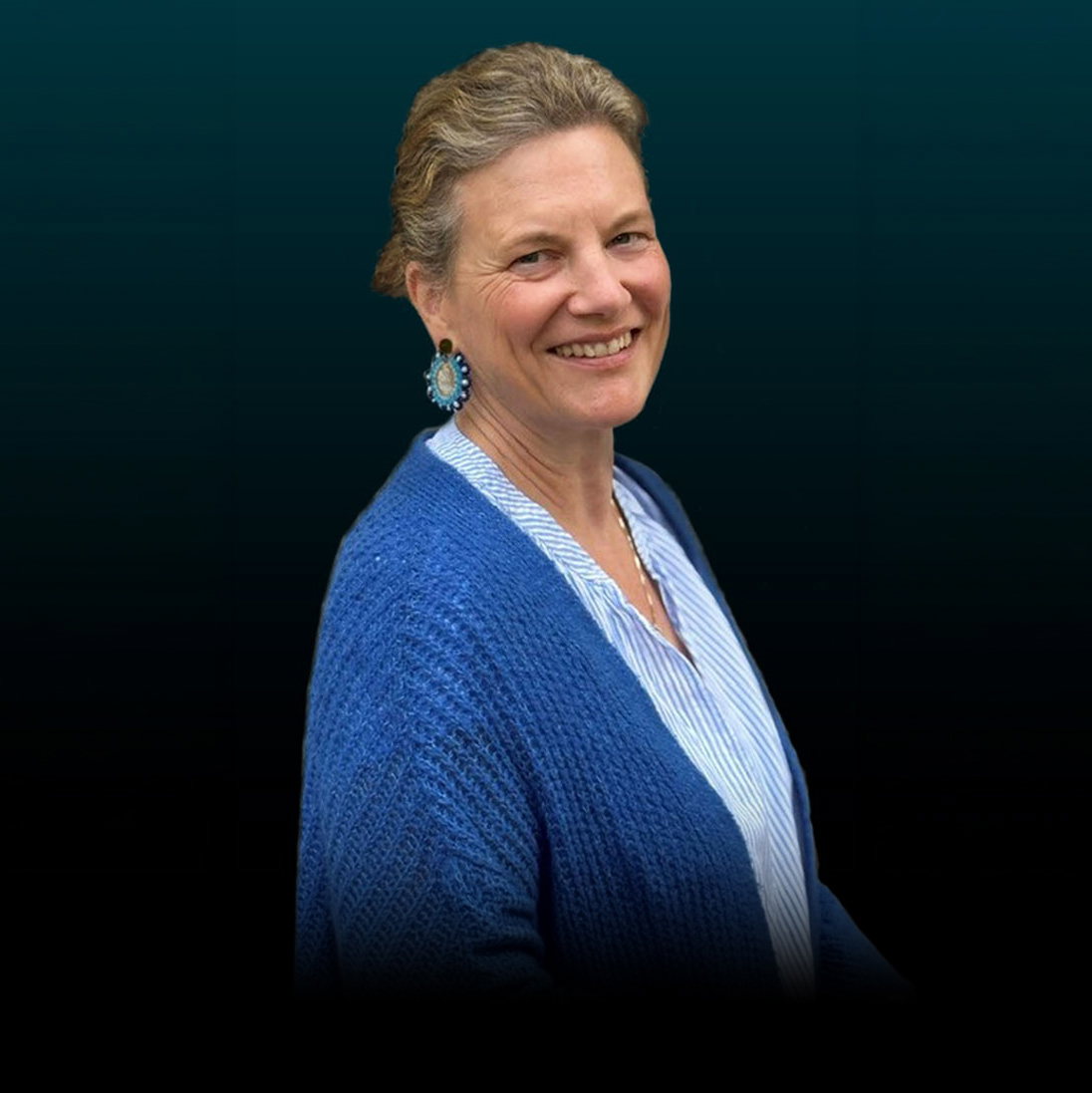 Freisteller von Annalena Köhler vor dunklem Hintergrund. Die Frau trägt eine dunkelblaue Wolljacke und eine hellblau gestreifte Bluse. Ihr Haar ist nach hinten gebunden.