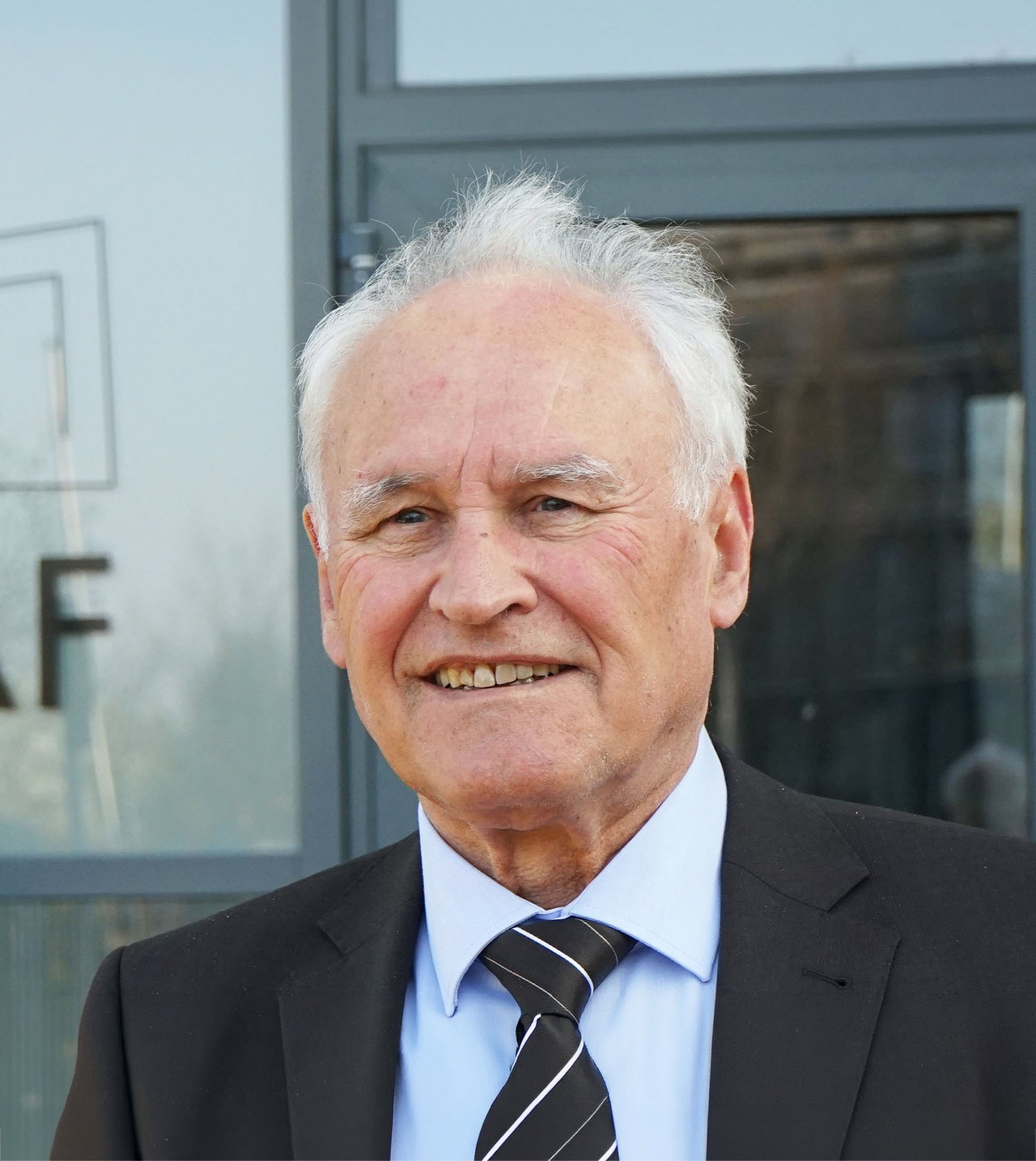Porträt von Erwin Huber im Anzug, im Hintergrund eine Glastür. Der Mann hat weißes Haar.
