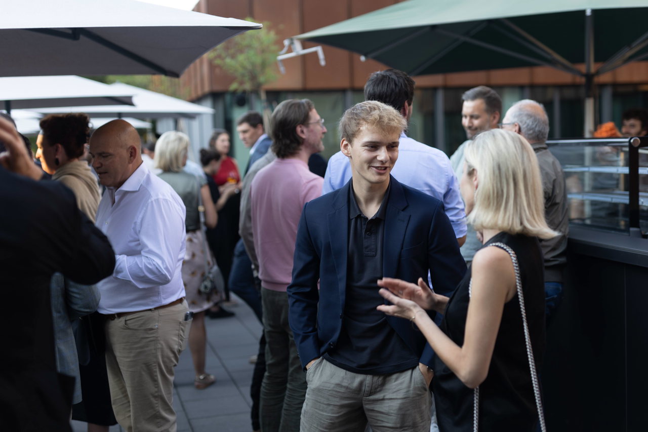 Gäste unterhalten sich beim sommerlichen Fest auf einer Terrasse mit Sonnenschirmen