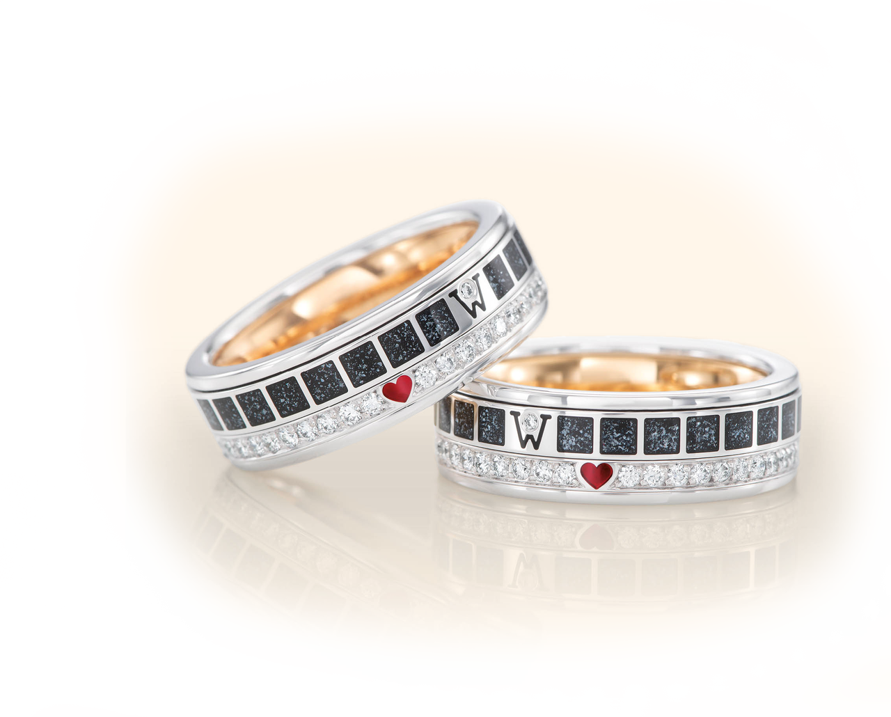 Zwei Wellendorff Ringe FREIHEIT IST aus Weißgold mit dunklen Kaltemaille-Feldern, kleinen Diamanten und einem roten Herz-Akzent.