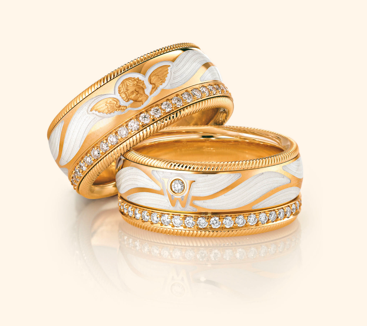Zwei goldene Wellendorff Ringe BESCHÜTZE MICH aus Gelbgold liegen übereinander auf einer reflektierenden Oberfläche.