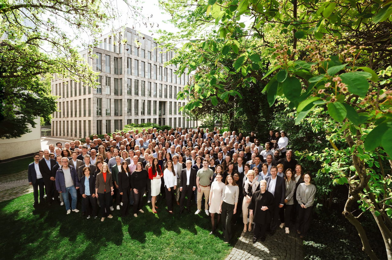 Das Team der LfA Förderbank Bayern. Die über 400 Mitarbeiterinnen und Mitarbeiter stehen vor einem Bürogebäude, posieren im begrünten Hof für ein Gruppenfoto.